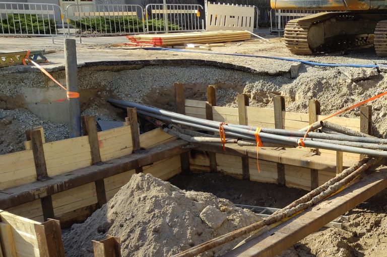 Many multicolored plastic pipes are in a trench of sand in perspective